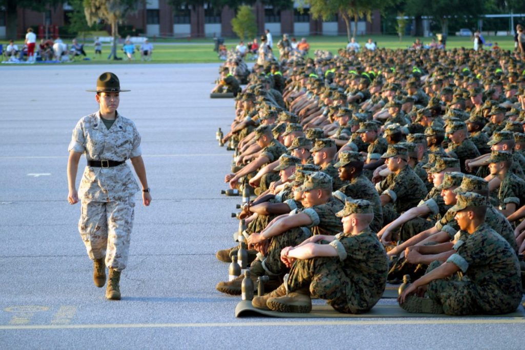 A US Marine Corps female Drill Instructor inspects the discipline of the recruits who are seated and lined up in platoon order during the annual Independence Day celebration at Parris Island. (Credit: U.S. National Archives)